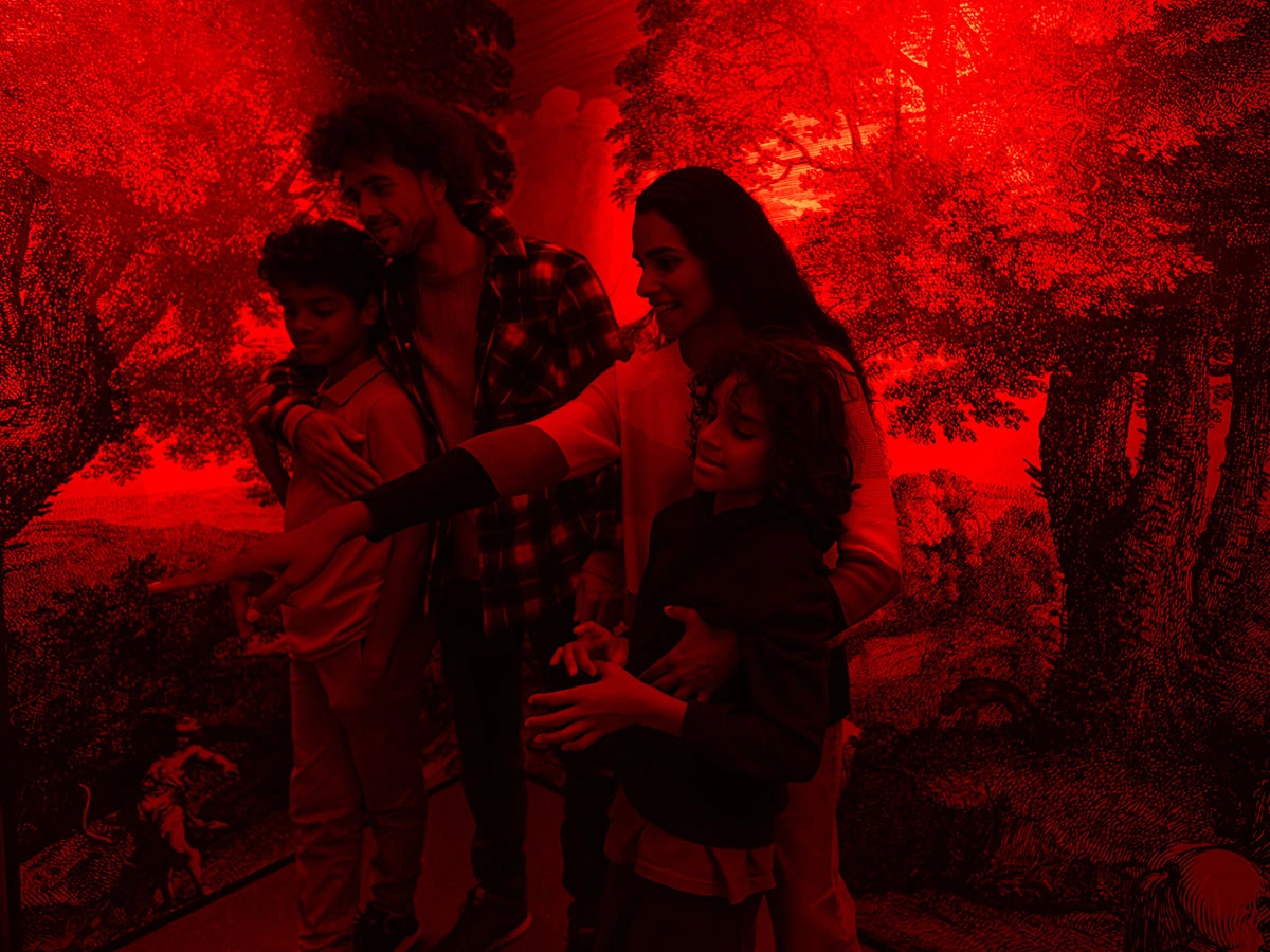 A family of four is standing in the Museum of Illusions RGB Room, lighted in red, looking and pointing at something out of the frame.