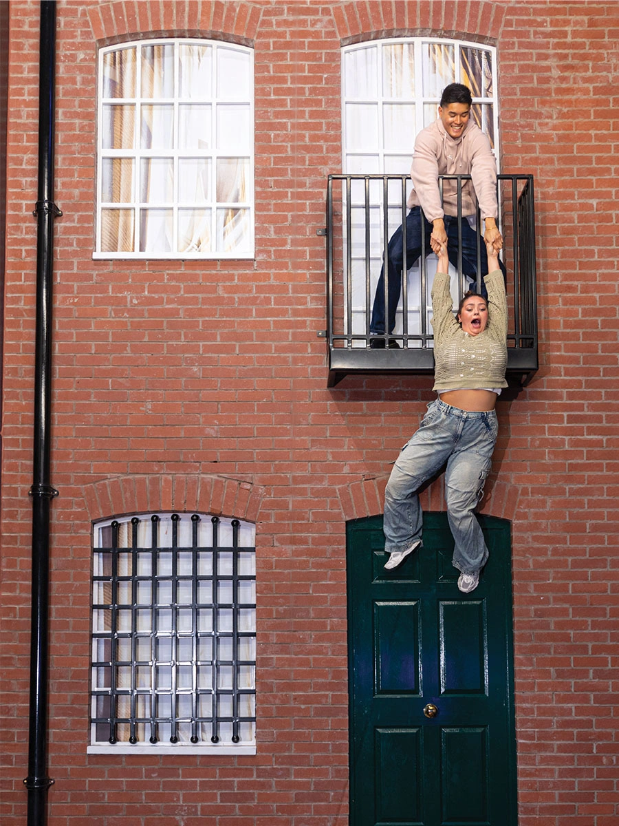 A man on a balcony holds a woman by her hands to prevent her fall, as a part of the Building Illusion at Museum of Illusions Manchester.