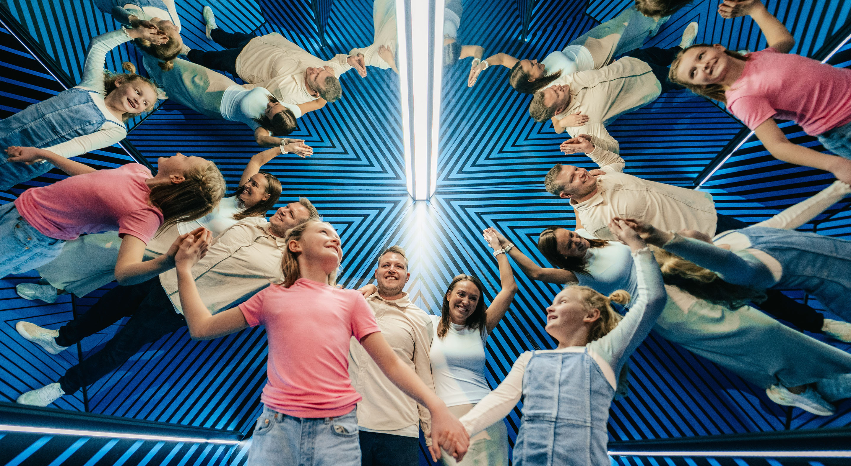 A group of visitors having fun surrounded by their own reflections in the Clone Room.
