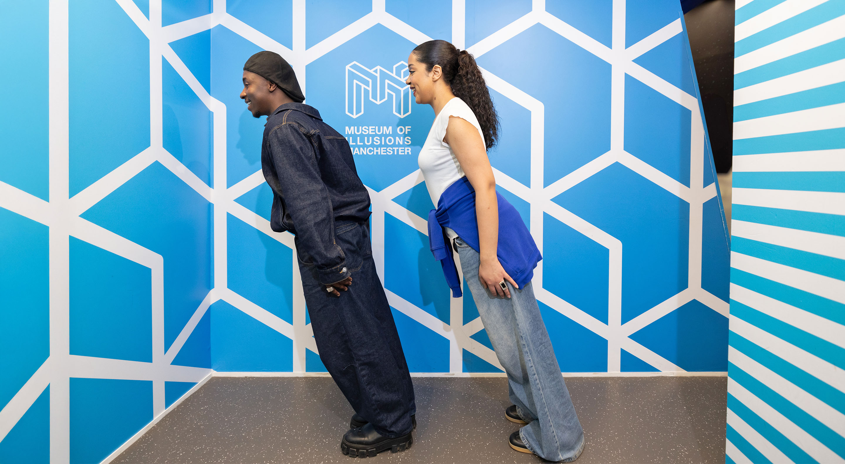 Two visitors leaning as if defying gravity in Museum of Illusions' Tilted Room.
