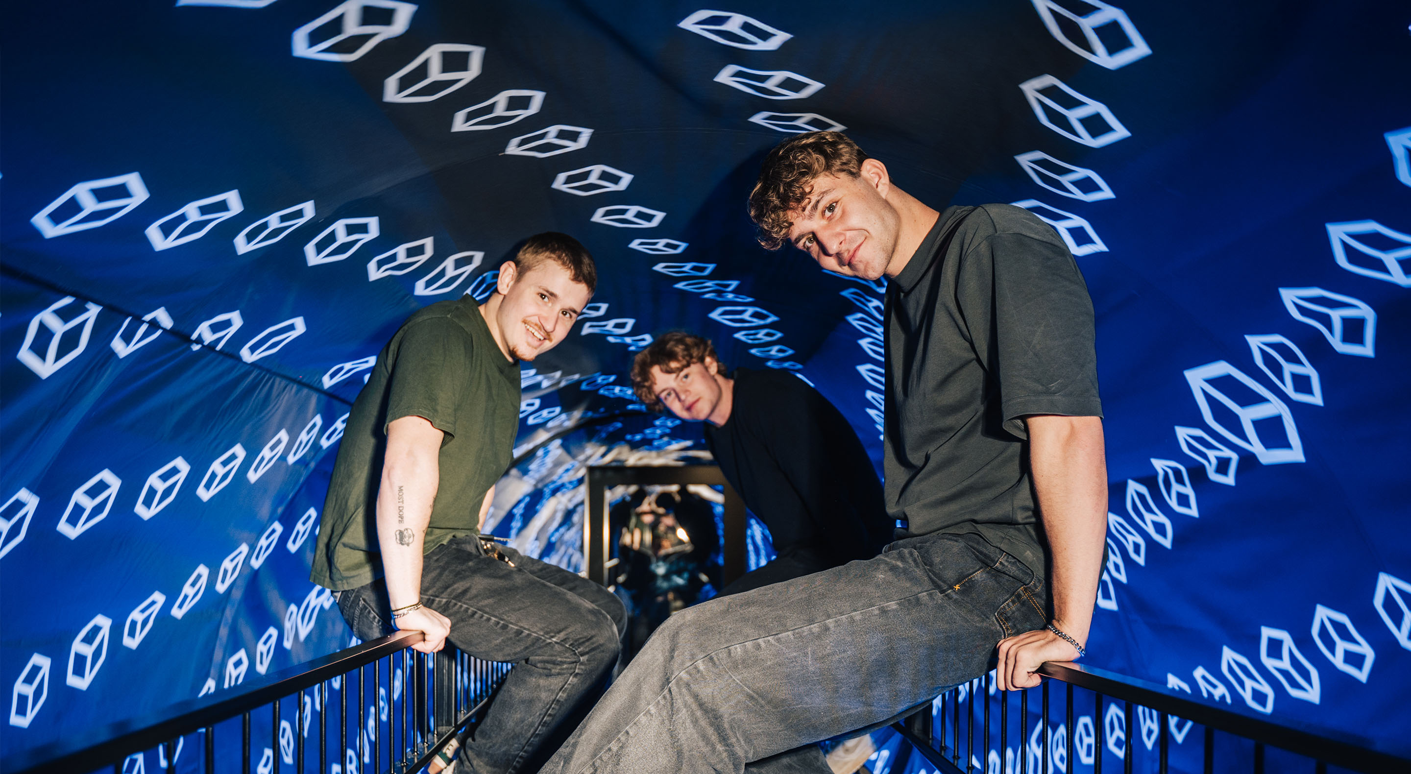 Three young visitors are sitting in the Vortex tunnel, surrounded by glow-in-the-dark signs.