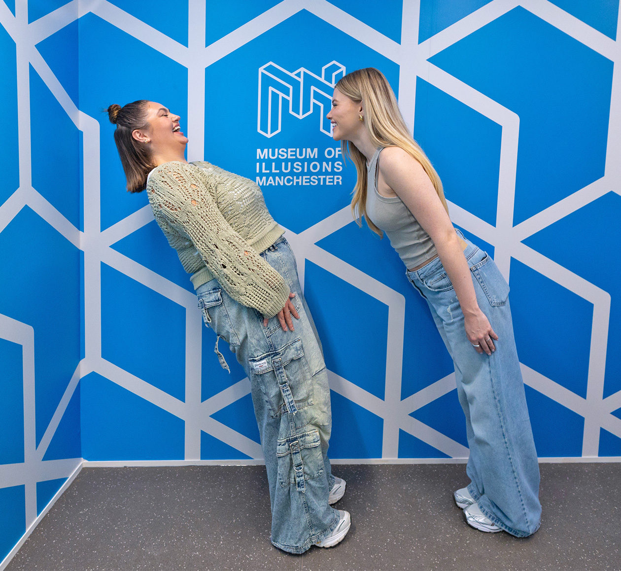 Two young women are leaning as if defying gravity at Museum of Illusions Tilted Room.